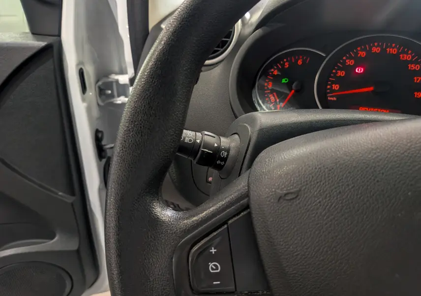 Vue intérieure rapprochée du volant et du tableau de bord du Renault Kangoo Express blanc, avec porte ouverte côté gauche visible.