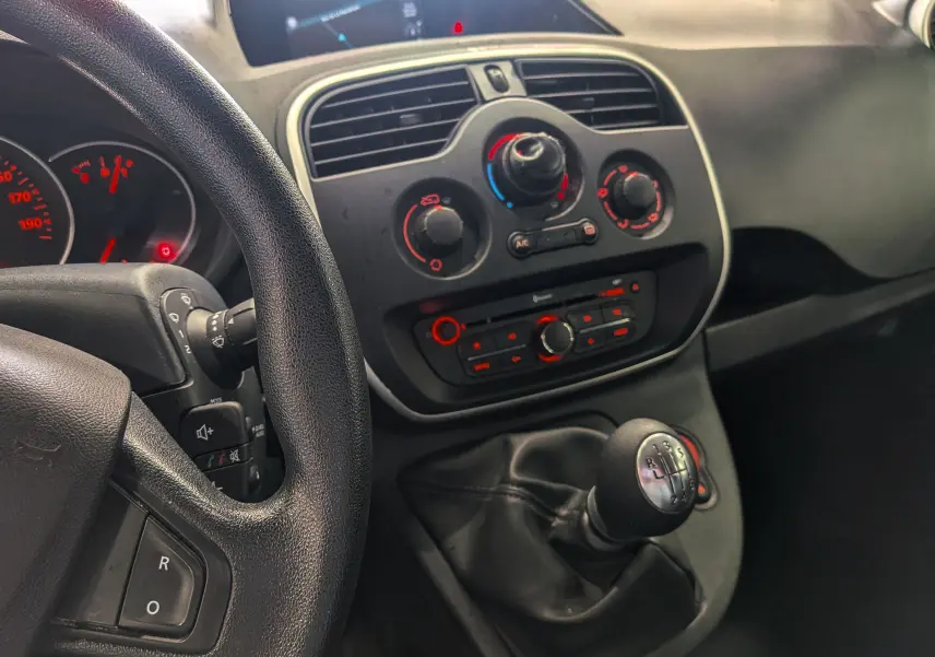 Vue intérieure centrée sur la console centrale et levier de vitesse manuel du Renault Kangoo Express blanc, avec commandes climatisation et radio.