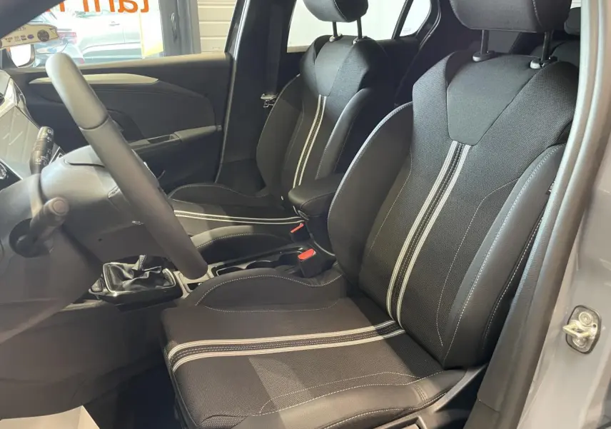Intérieur avant droit de l’Opel Corsa gris, sièges sport noirs avec bandes blanches et volant cuir synthétique.