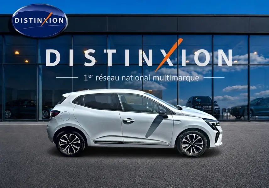 Profil droit d'une Renault Clio V gris rafale avec jantes alu et poignées ton carrosserie devant une vitrine Distinxion.