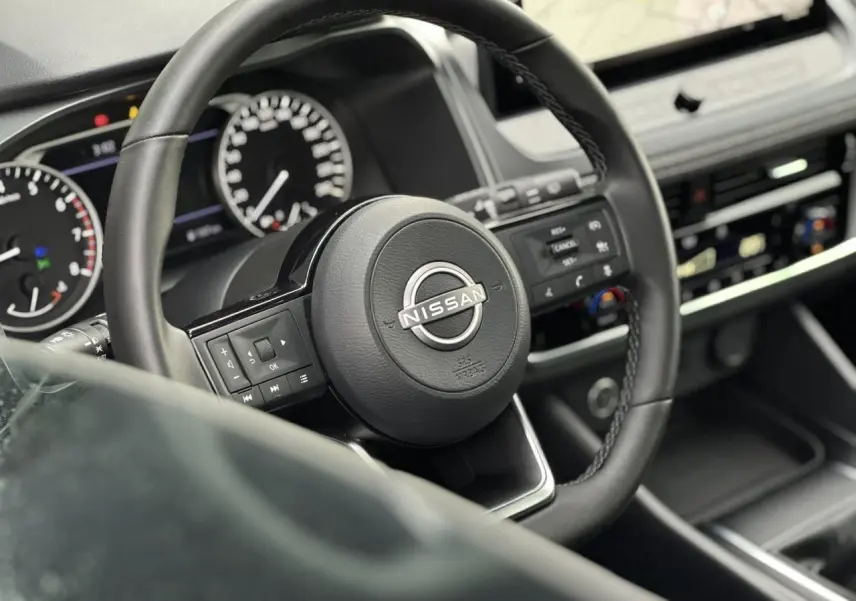 Vue rapprochée du volant noir du Nissan Qashqai 2024 avec commandes intégrées et tableau de bord digital.