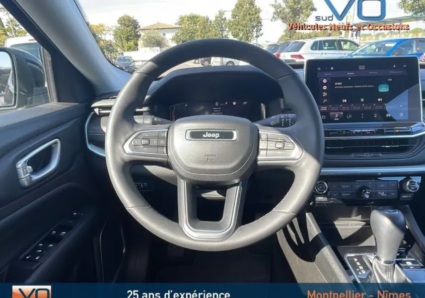 Vue intérieure centrée sur le volant Jeep noir et le tableau de bord avec écran tactile du Compass 2023.