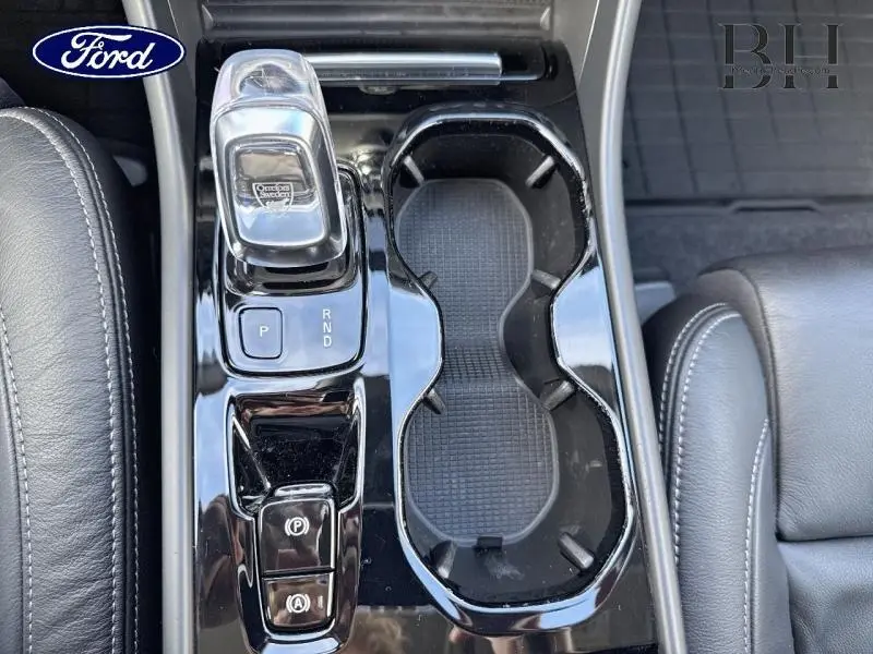 Vue plongeante sur la console centrale noire du Volvo XC40 bleu Denim, avec levier de vitesses transparent et porte-gobelets.