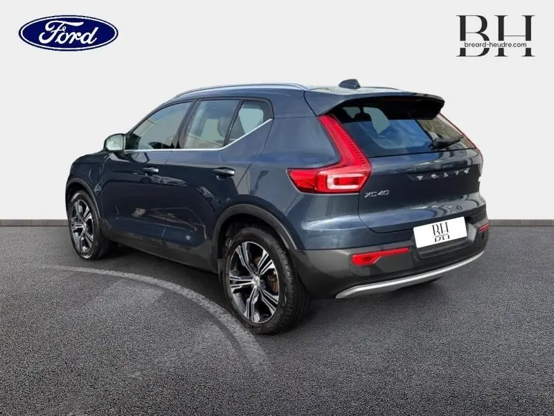 Vue 3/4 arrière droite d'un Volvo XC40 bleu Denim avec feux arrière en forme de L et jantes alliage distinctives.