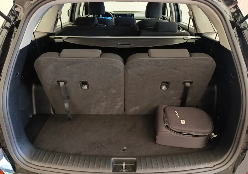 Coffre ouvert d’un KIA Sorento noir 2023, vue arrière, avec troisième rangée de sièges relevée et sac KIA noir posé.