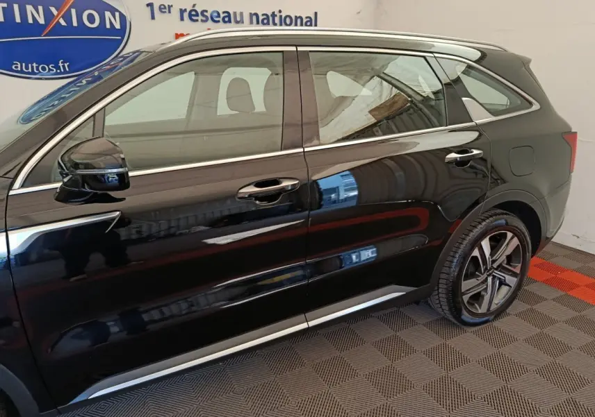 Vue latérale droite d'un KIA Sorento noir 2023 hybride rechargeable, avec jantes alliage et barres de toit chromées.