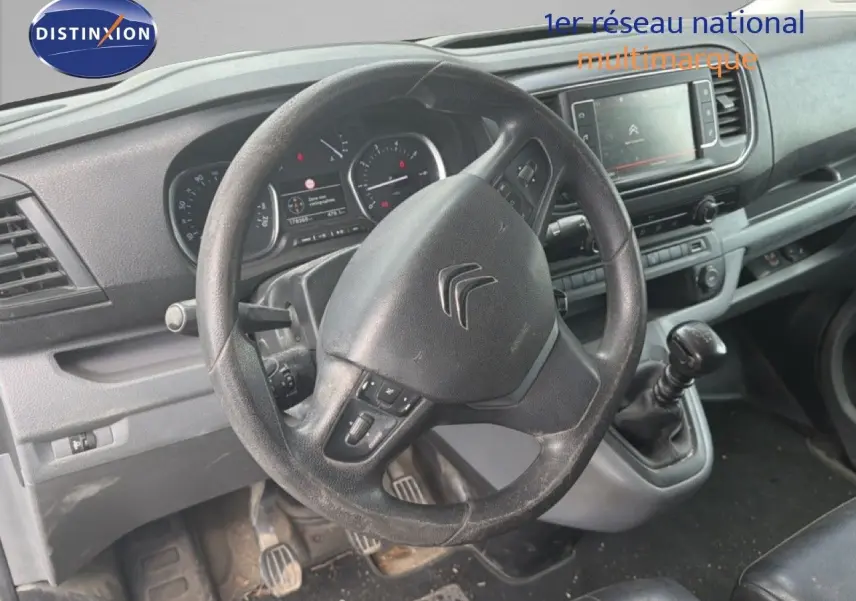 Vue intérieure du poste de conduite du Citroën Jumpy blanc, volant et levier de vitesse manuelle visibles de face.