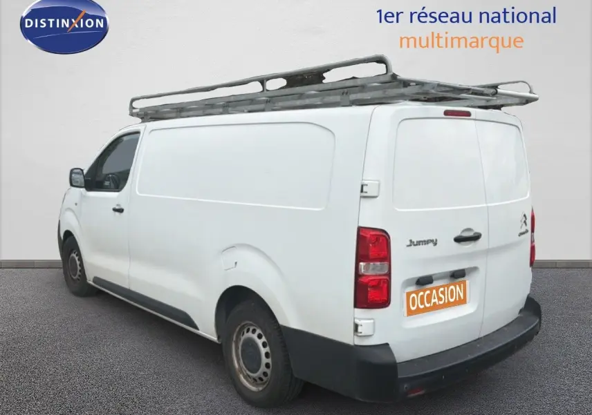 Vue 3/4 arrière gauche d’un Citroën Jumpy blanc avec galerie de toit et marquage "occasion" sur la porte arrière.