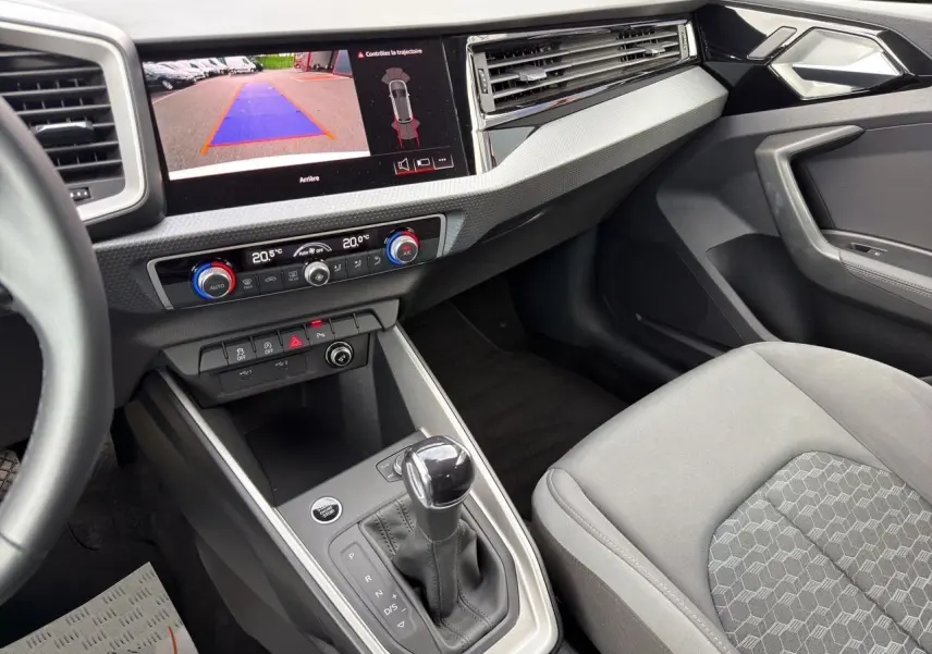Vue intérieure côté passager de l'Audi A1 Sportback blanche, avec console centrale et écran de caméra de recul allumé.