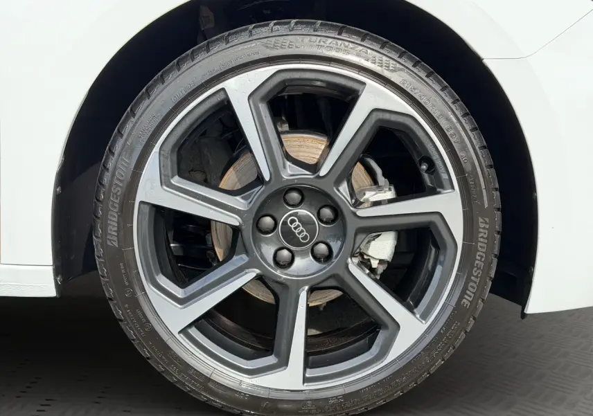 Gros plan sur la roue avant droite d'une Audi A1 Sportback blanche avec jante alliage gris foncé à design moderne.