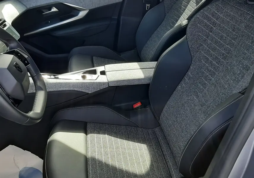 Vue intérieure côté conducteur du Peugeot 5008 Hybrid 2025, sièges tissu gris et cuir noir avec console centrale assortie.