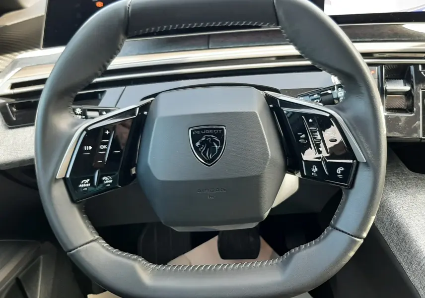 Vue rapprochée du volant cuir noir du Peugeot 5008 Hybrid 2025 avec commandes tactiles et tableau de bord numérique.