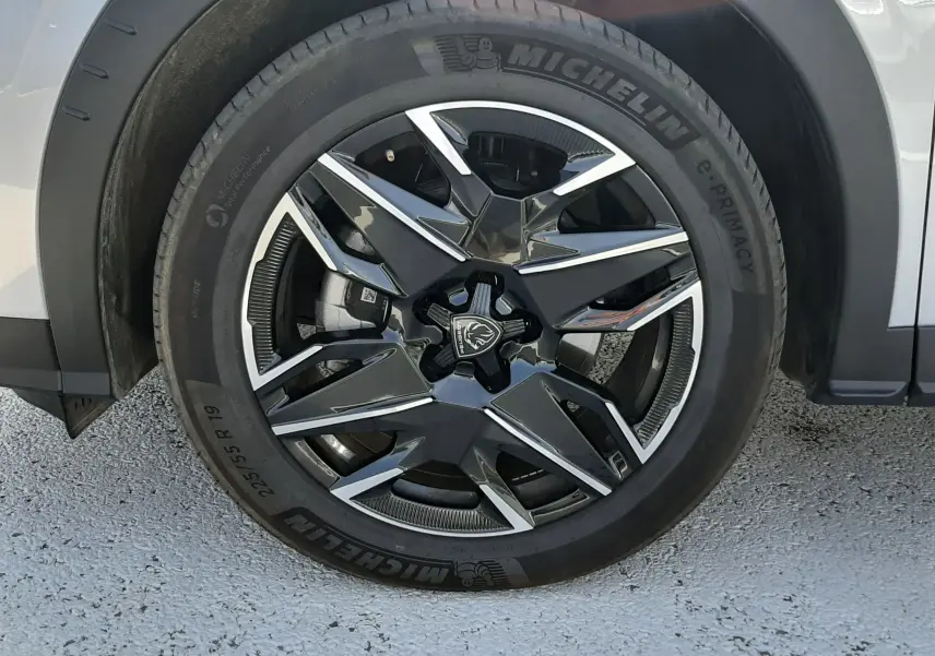 Gros plan sur la roue avant gauche du Peugeot 5008 gris Artense, jante alliage noire et argent avec logo Peugeot central.