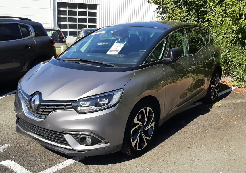 Renault Scenic IV gris cassiopée avec toit noir, vu en 3/4 avant droit sur parking extérieur ensoleillé.