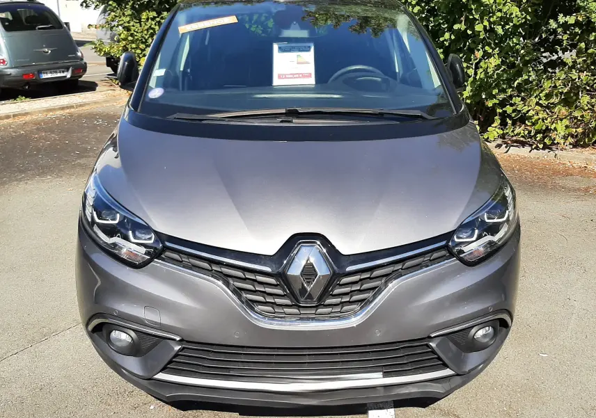 Vue avant d'un Renault Scénic IV gris Cassiopée avec toit noir, calandre marquée et phares LED allumés.