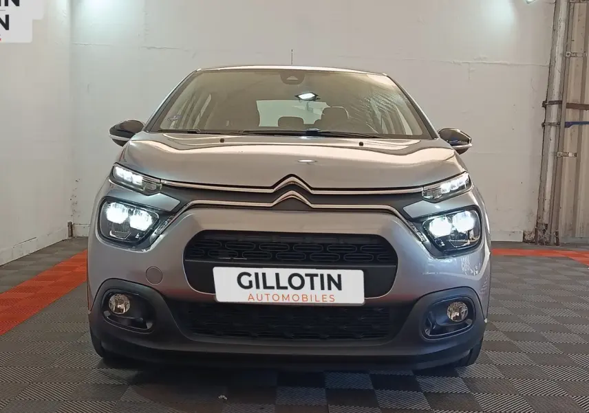 Vue frontale d'une Citroën C3 gris foncé 2024 avec phares LED allumés dans un showroom.