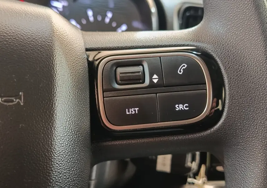 Gros plan sur les commandes gauche du volant noir de la Citroën C3 2024, boutons LIST, SRC et téléphone.