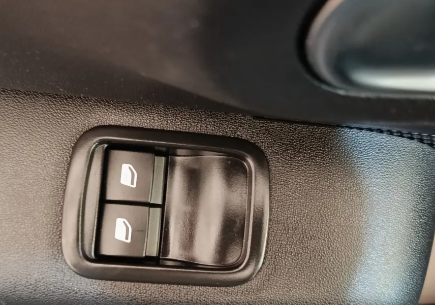 Gros plan sur les commandes des vitres électriques côté conducteur d’une Citroën C3 gris foncé, intérieur voiture.