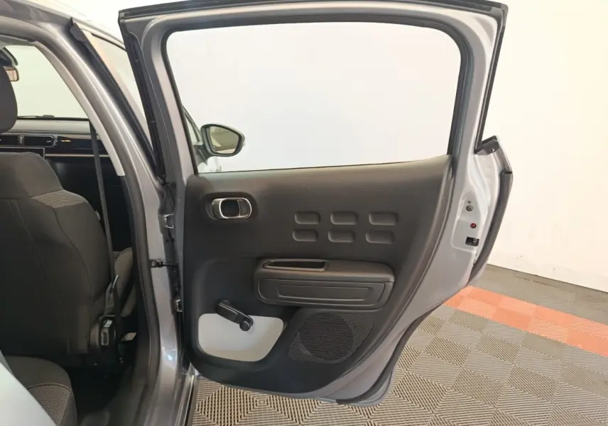 Vue intérieure côté gauche de la porte arrière ouverte d'une Citroën C3 2024 gris foncé, avec manivelle de vitre visible.