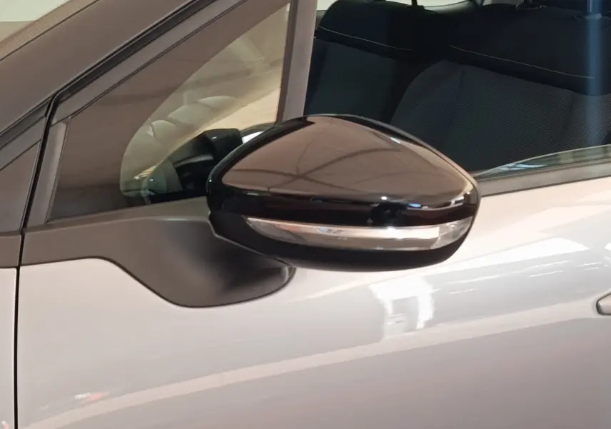 Gros plan sur le rétroviseur noir brillant côté gauche d'une Citroën C3 gris foncé avec partie de la porte visible.