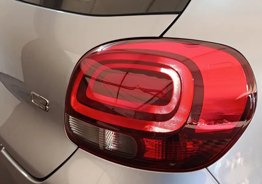 Gros plan sur le feu arrière droit rouge et le logo C3 d'une Citroën C3 gris foncé vue de l'arrière.