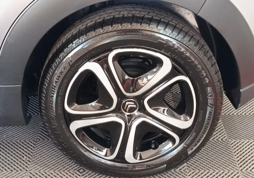Gros plan sur la roue avant droite d'une Citroën C3 gris foncé avec jante alliage noire et argentée.