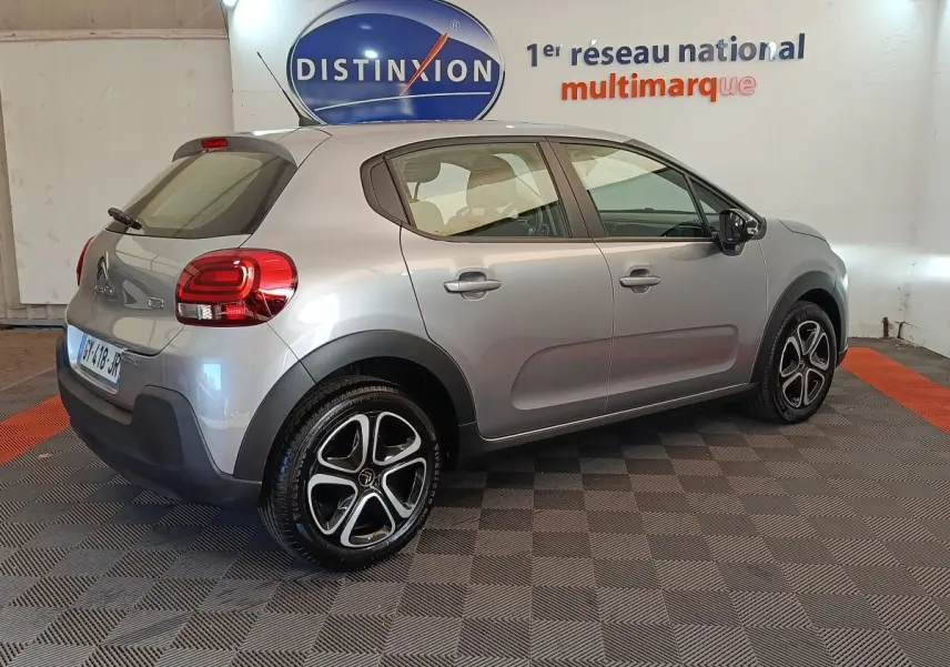 Vue 3/4 arrière droite d'une Citroën C3 gris foncé 2024 avec jantes noires et rouges, stationnée en intérieur.