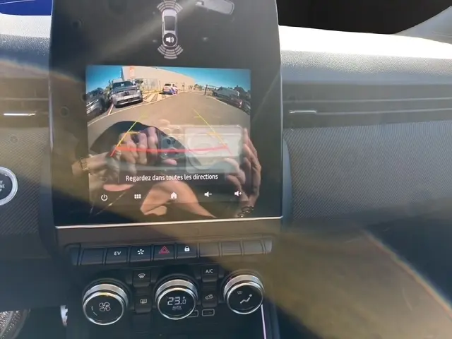 Écran tactile central affichant la caméra de recul d’une Renault Clio gris clair, avec commandes climatisation en dessous.
