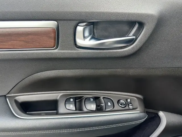 Gros plan sur la porte côté gauche du Renault Koleos noir, montrant la poignée, les commandes des vitres et un insert bois.