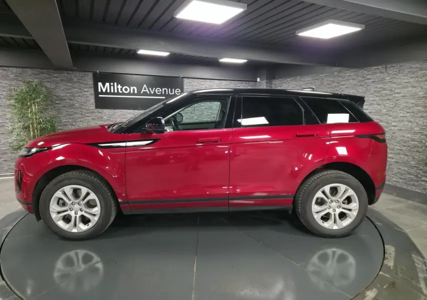 Profil droit d'un Range Rover Evoque rouge avec toit noir contrasté dans un showroom intérieur.