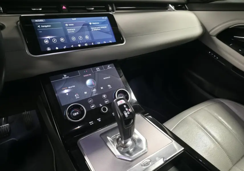 Intérieur du Range Rover Evoque 2019, vue sur la console centrale avec levier de vitesse et écran tactile, sellerie cuir claire.