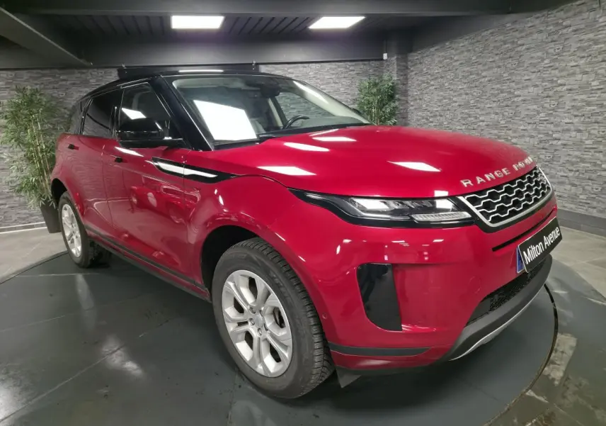 Range Rover Evoque rouge vue 3/4 avant droit avec toit noir et calandre distinctive en intérieur showroom.