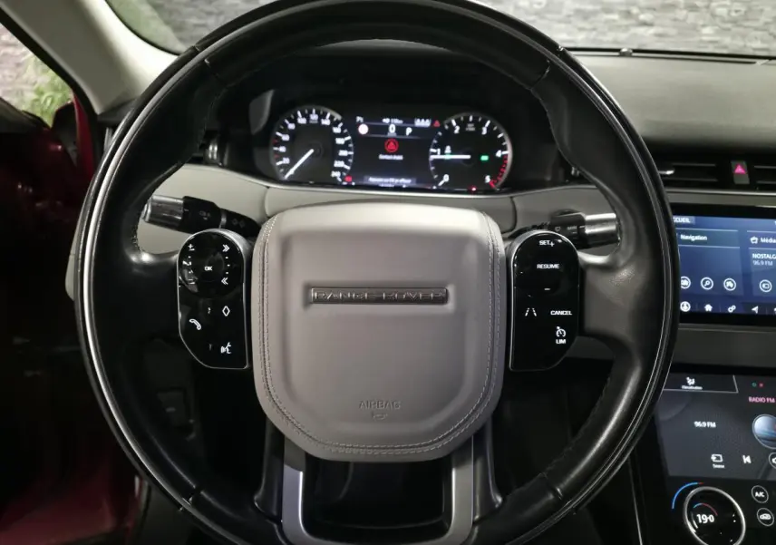 Vue rapprochée du volant cuir noir et gris avec logo Range Rover, tableau de bord et écran tactile du Range Rover Evoque rouge 2019.