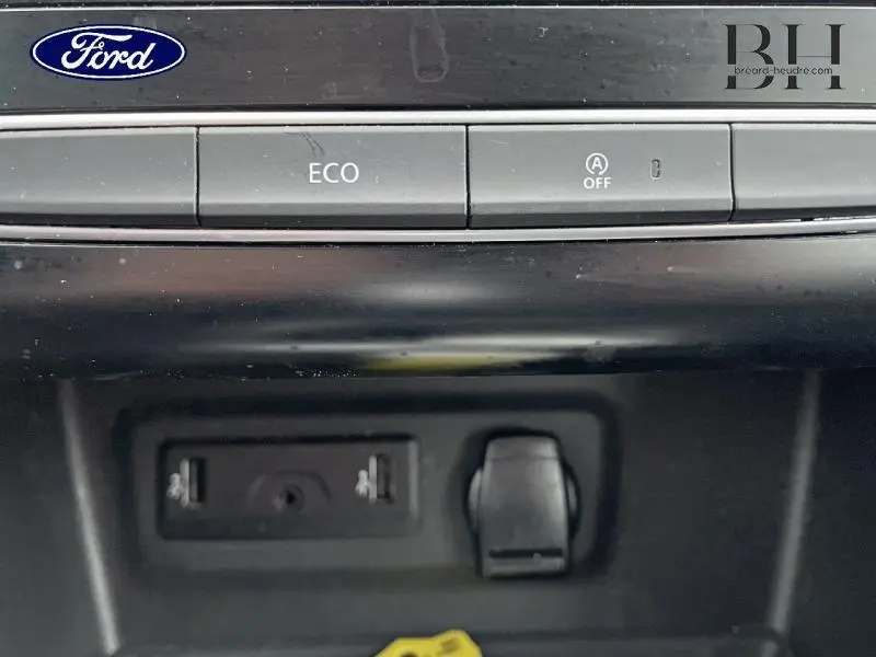 Gros plan sur la console centrale noire avec boutons ECO et désactivation arrêt auto, prises USB et prise 12V visibles.