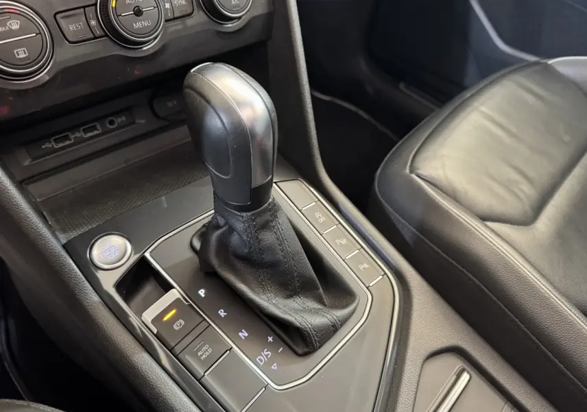 Vue rapprochée de la console centrale du Volkswagen Tiguan Allspace gris foncé, montrant le levier de vitesse automatique et les commandes environnantes.