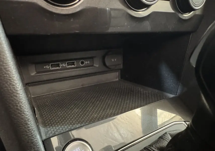 Gros plan sur la console centrale noire du Volkswagen Tiguan Allspace, montrant prises USB, prise 12V et bouton démarrage.