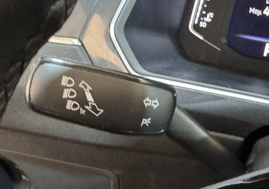 Gros plan sur la manette de clignotants noire à gauche du volant du Volkswagen Tiguan Allspace gris foncé, avec pictogrammes blancs.