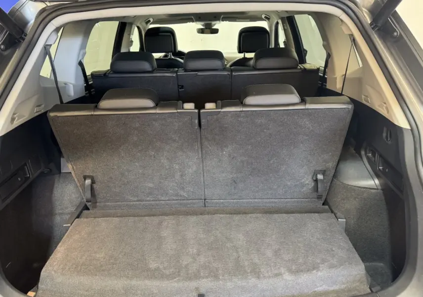 Vue arrière du coffre du Volkswagen Tiguan Allspace gris foncé avec troisième rangée de sièges relevée et banquette arrière visible.