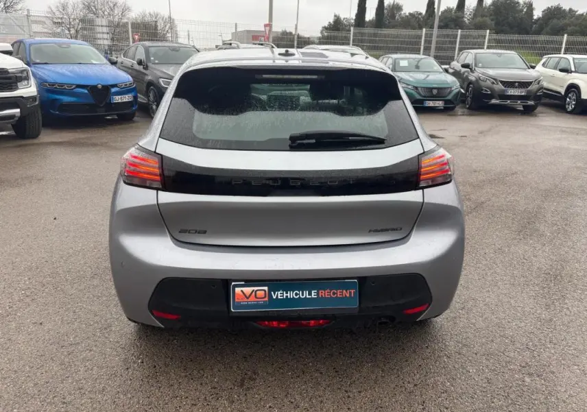 Vue arrière d'une Peugeot 208 Hybrid gris 2025 avec feux LED allumés sur un parking humide.