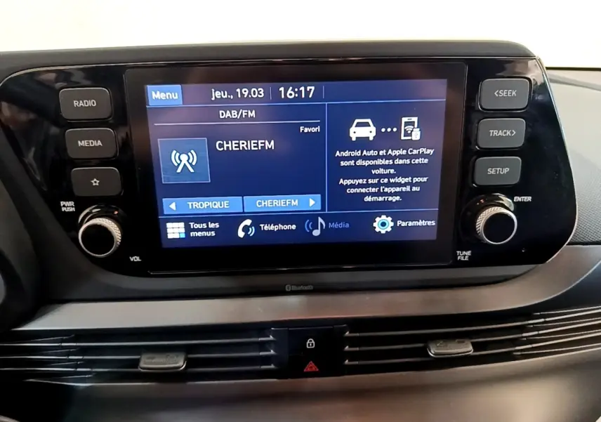 Vue rapprochée de l'écran tactile central noir de la Hyundai i20 2022 affichant la radio et options connectées.