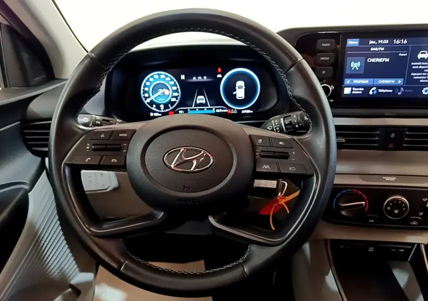 Vue intérieure centrée sur le volant cuir multifonctions et tableau de bord numérique de la Hyundai i20 gris clair 2022.