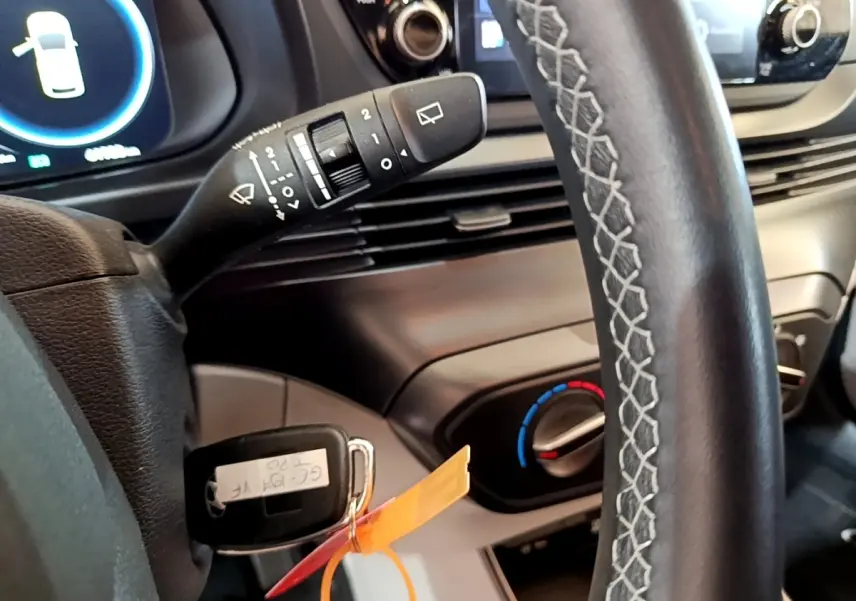 Gros plan sur le volant cuir et la clé insérée du Hyundai i20 gris clair, avec commandes d’essuie-glace et réglage clim visible.