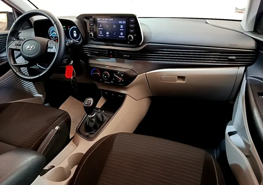 Vue intérieure de la Hyundai i20 2022, tableau de bord gris clair avec volant cuir multifonctions et boîte manuelle.