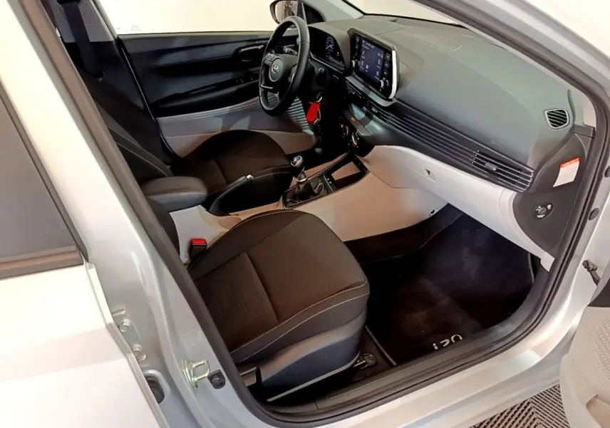 Vue intérieure côté conducteur de la Hyundai i20 gris clair 2022, avec tableau de bord moderne et volant multifonctions cuir.