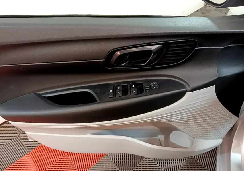 Vue intérieure du panneau de porte côté conducteur de la Hyundai i20 gris clair, avec commandes électriques et poignée noire.