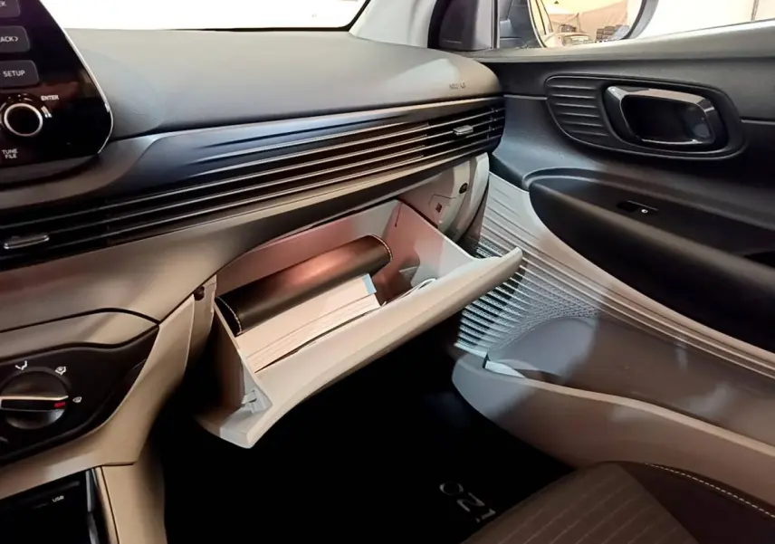 Vue intérieure côté passager de la Hyundai i20 2022 gris clair, boîte à gants ouverte avec documents visibles.