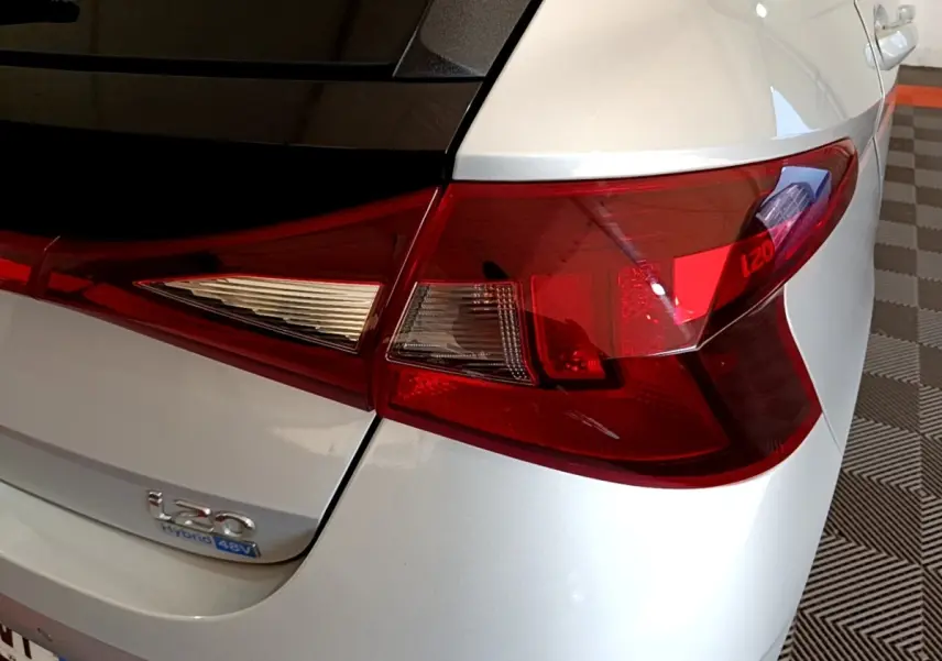 Gros plan sur le feu arrière droit rouge et blanc d’une Hyundai i20 gris clair hybride avec logo i20 visible.