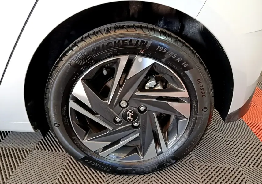 Gros plan sur la roue arrière droite d'une Hyundai i20 gris clair, avec jante alliage au design géométrique.