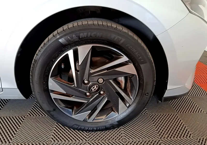 Gros plan sur la roue avant gauche gris clair d'une Hyundai i20 2022 avec jante alliage noire et argentée.