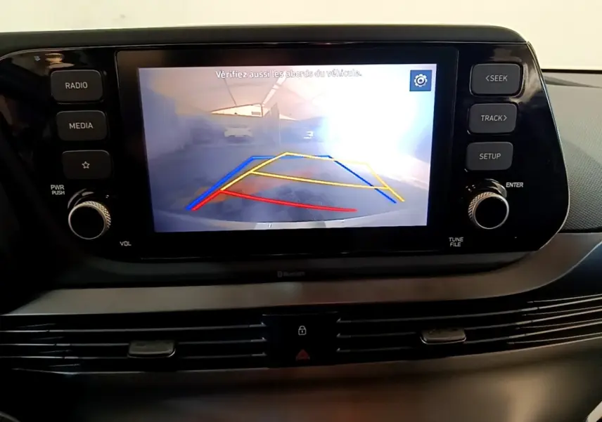 Écran tactile central affichant la caméra de recul avec guidage coloré dans l’habitacle d’une Hyundai i20 gris clair.